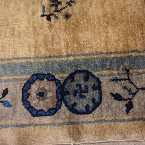 Close up of medium-pile tan rug border with blue floral and circular gray patterns.