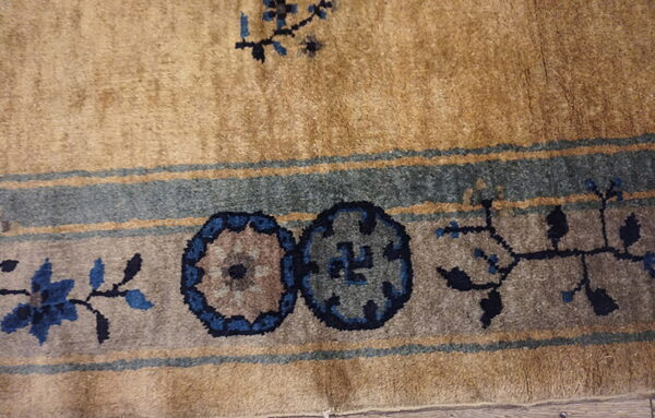 Close up of medium-pile tan rug border with blue floral and circular gray patterns.