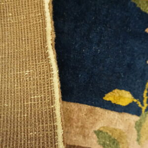 Coarse tan backing meets a dark blue pile rug featuring light beige and green floral patterns.