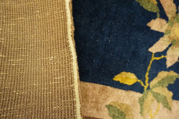 Coarse tan backing meets a dark blue pile rug featuring light beige and green floral patterns.