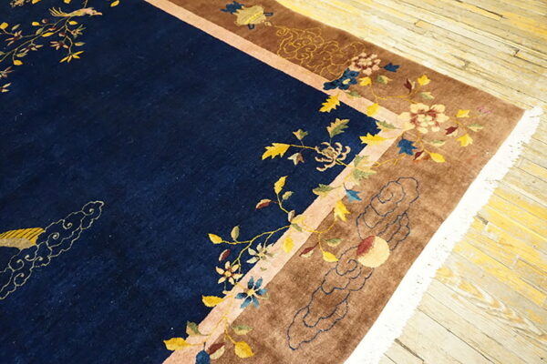Plush navy rug featuring a colorful bird and floral design, surrounded by a tan border on wood floors.