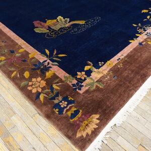 High-pile blue rug with botanical patterns in a brown border lies on distressed light wood plank flooring.