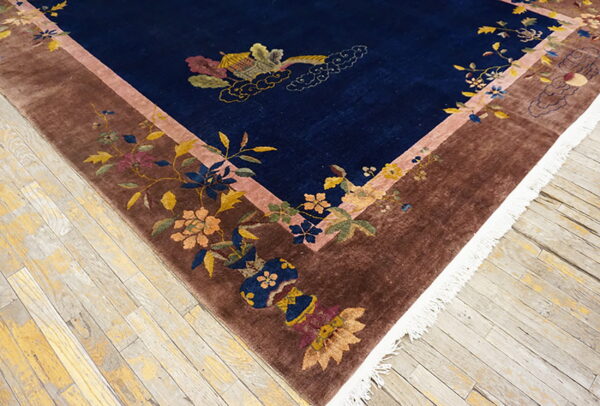 High-pile blue rug with botanical patterns in a brown border lies on distressed light wood plank flooring.