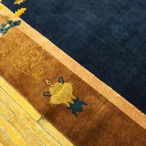 Plush navy and brown bordered rug with gold motifs rests on heavily distressed yellow wood planks.