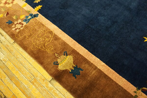 Plush navy and brown bordered rug with gold motifs rests on heavily distressed yellow wood planks.