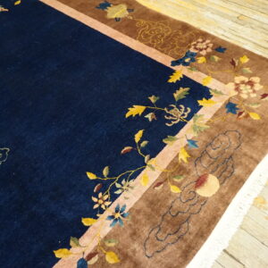 Navy blue high-pile rug featuring colorful floral vines, birds, and a wide brown border on worn wooden floorboards.