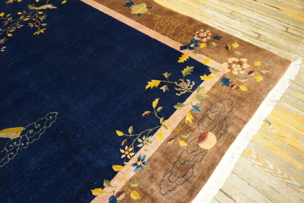 Navy blue high-pile rug featuring colorful floral vines, birds, and a wide brown border on worn wooden floorboards.