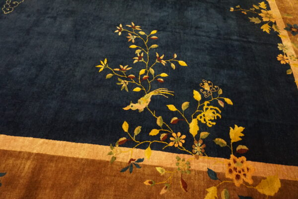 Plush dark blue rug with a yellow floral and bird motif bordering a wide brown band.