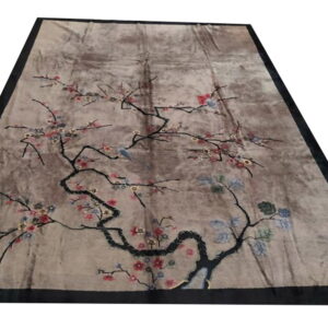 Mottled taupe rug with a dark border features an ornate black branch, pink flowers, and a light blue bird.