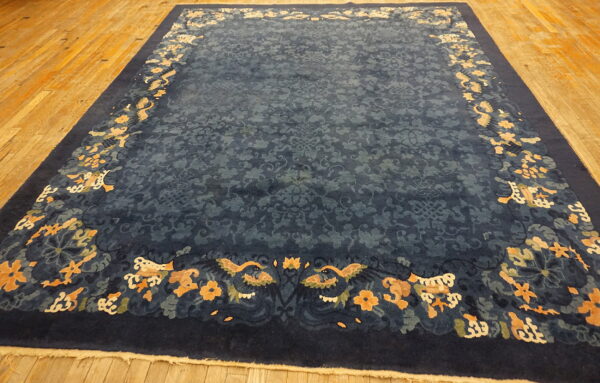 Navy blue rug with a subtle field pattern and a wide border of apricot and cream motifs on a wood floor.