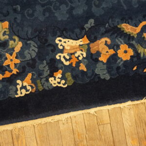 Navy blue high-pile rug with orange and cream motifs resting on hardwood flooring.