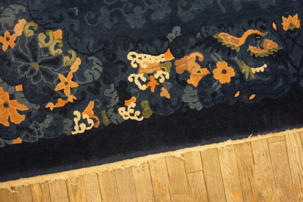 Navy blue high-pile rug with orange and cream motifs resting on hardwood flooring.