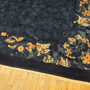 Plush navy blue rug featuring a dense tone-on-tone field and gold floral border on wood floors.