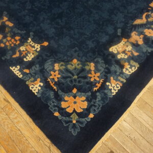 Dark blue patterned rug with contrasting peach and cream designs rests on worn light hardwood flooring.