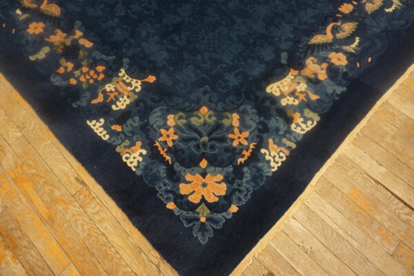 Dark blue patterned rug with contrasting peach and cream designs rests on worn light hardwood flooring.