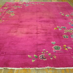 A magenta rug with a lustrous pile features colorful floral and vine borders lying on hardwood plank flooring.
