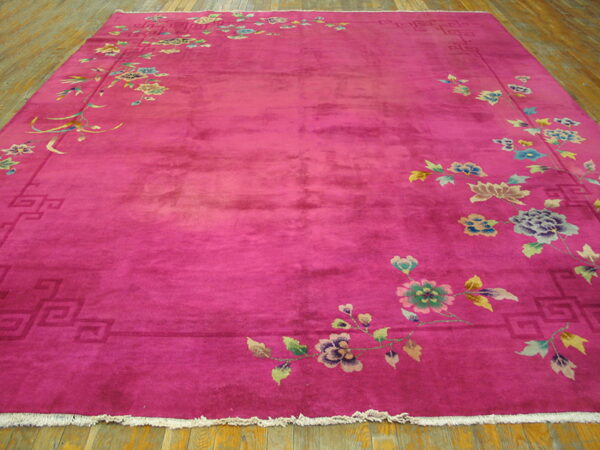 A magenta rug with a lustrous pile features colorful floral and vine borders lying on hardwood plank flooring.