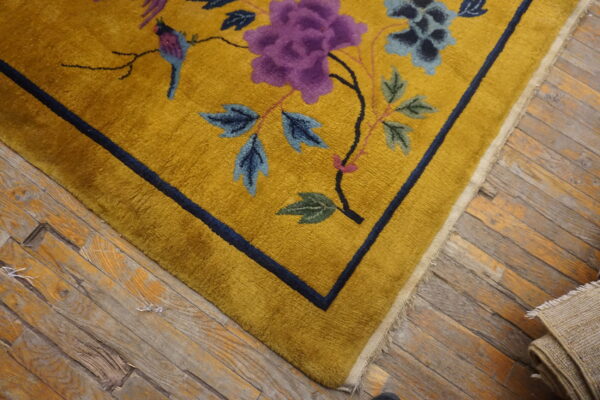 Mustard high-pile rug featuring purple and blue floral designs and a bird on distressed wood flooring.
