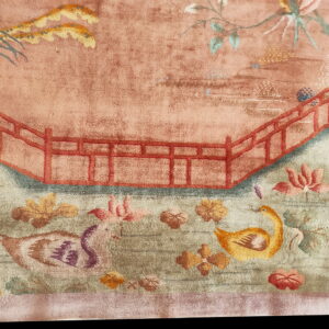 Faded pink and green rug detail with a red railing, stylized birds, and floral garden patterns.