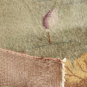 Detail view of a rug showing sage green pile, mauve pattern, and tightly woven pink selvedge backing.