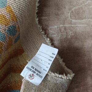 A beige low-pile rug is rolled, revealing its densely woven backing with geometric gold and blue patterns.
