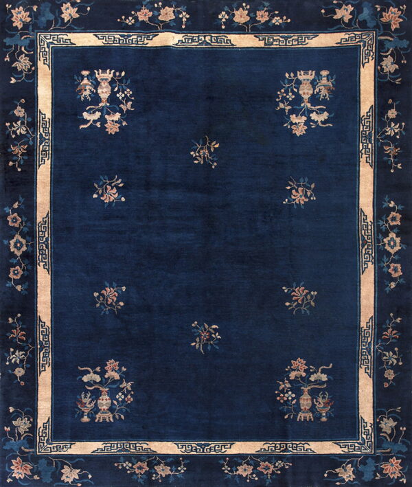 Dark blue rug featuring floral vases and scatter motifs, framed by a thick tan border with geometric details.