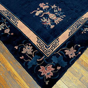 Navy blue rug corner on wood flooring, detailed with pale pink florals and a thick geometric border.