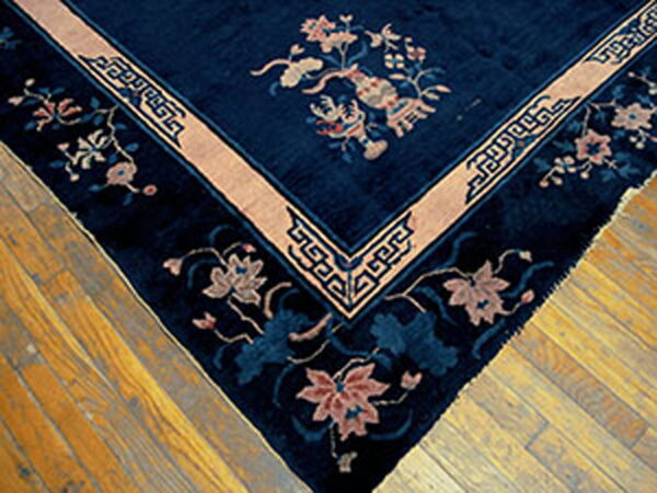 Navy blue rug corner on wood flooring, detailed with pale pink florals and a thick geometric border.