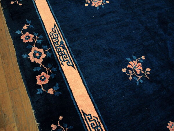 Deep blue high-pile rug featuring peach floral motifs and geometric borders rests on wood plank flooring.