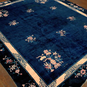 Navy blue rug with peach floral sprays and key pattern borders lying on polished wood flooring.