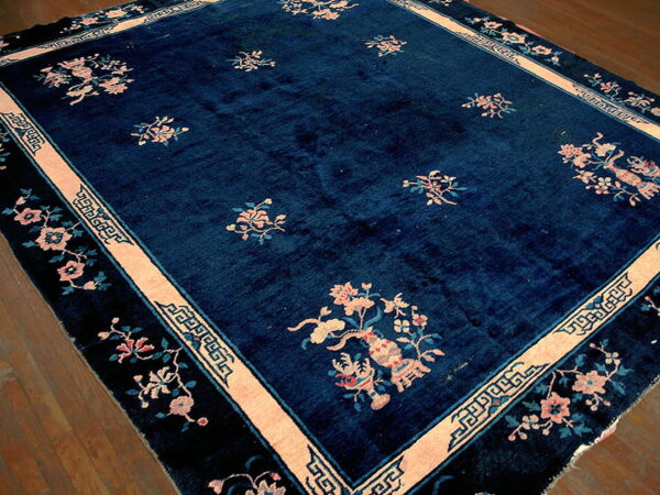 Navy blue rug with peach floral sprays and key pattern borders lying on polished wood flooring.