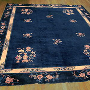 Rectangular dark blue rug with contrasting peach and pink floral patterns laid on wood floorboards.