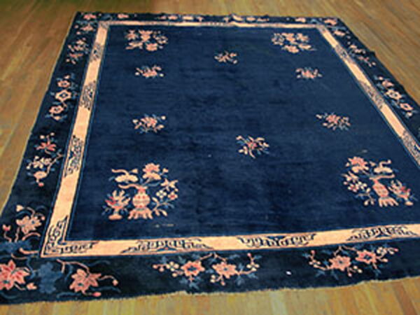 Rectangular dark blue rug with contrasting peach and pink floral patterns laid on wood floorboards.