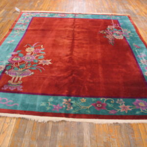 Rectangular red and teal rug with pink floral corner motifs displayed on rustic wood flooring.