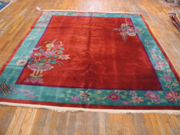 Rectangular red and teal rug with pink floral corner motifs displayed on rustic wood flooring.