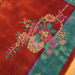 Detailed view of a high-pile rug featuring a floral basket motif, rust field, and wide teal border.