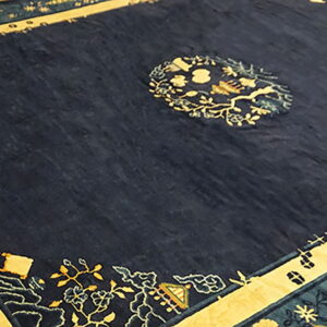 Dark blue rug displaying ornate yellow and teal borders and a central medallion on wood flooring.