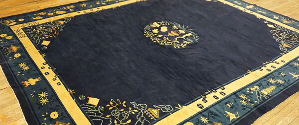 Dark blue rug displaying ornate yellow and teal borders and a central medallion on wood flooring.