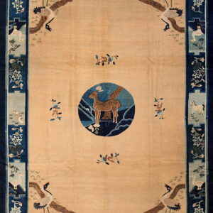 Tan rug with a navy blue border featuring detailed corner cranes and animal motifs in light blue cartouches.