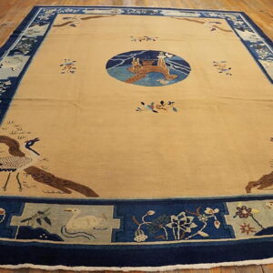 Large beige rug with a dark blue pictorial border featuring cranes and flowers on a polished wooden floor.