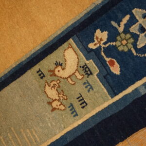 Low-pile rug detail showing a golden field, blue borders, and stylized bird patterns on wood flooring.