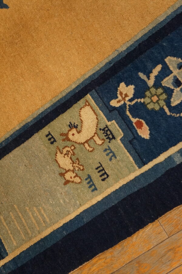 Low-pile rug detail showing a golden field, blue borders, and stylized bird patterns on wood flooring.