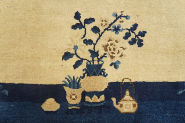 Detail of a high-pile rug showing blue and brown flowers in vases above a dark navy border.