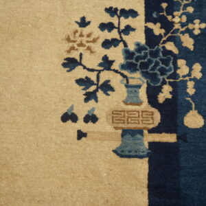 Beige rug featuring a dark blue and brown floral vase design against wood plank flooring.