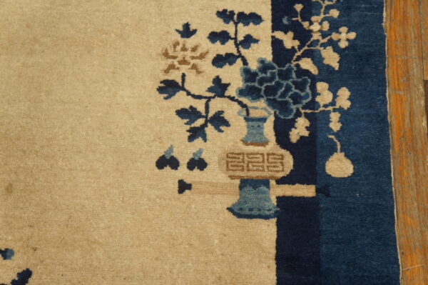Beige rug featuring a dark blue and brown floral vase design against wood plank flooring.