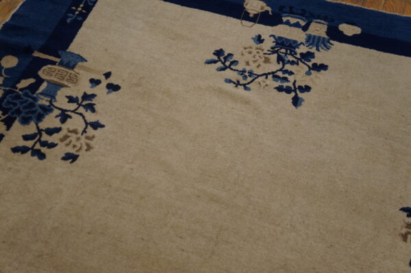 Beige rug featuring a dark blue border and stylized blue floral patterns on a light brown wooden floor.