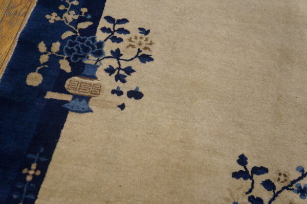 Plush beige rug with dark blue and brown floral patterns and border detail on wood flooring.