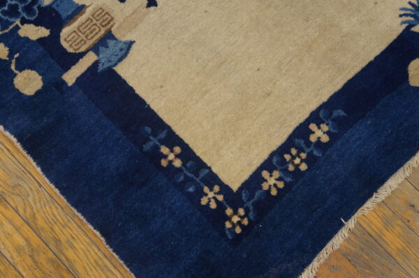 A high-pile rug corner features a navy blue border, beige field, and stylized floral motifs on wood planks.