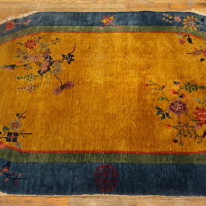 Gold oval rug with an ornate floral pattern and a wide blue and green border rests on wood planks.