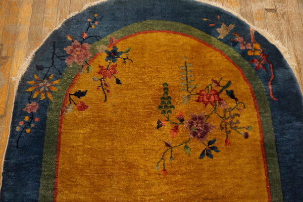 Mustard yellow rug with blue and green borders displays colorful floral motifs on distressed wood flooring.